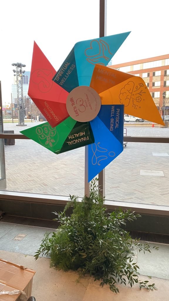 Multicolored scenic pinwheel form displayed beside greenery.