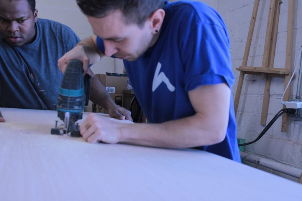 Two workshop team members using a handheld router on a large panel.
