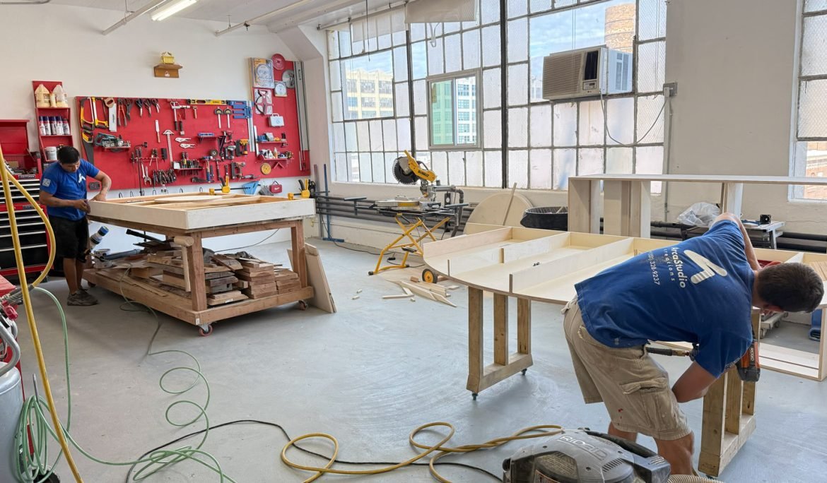 Two people working on large rectangular components at workshop benches.