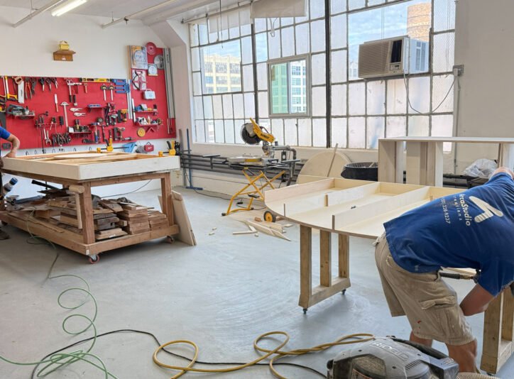 Two people working on large rectangular components at workshop benches.