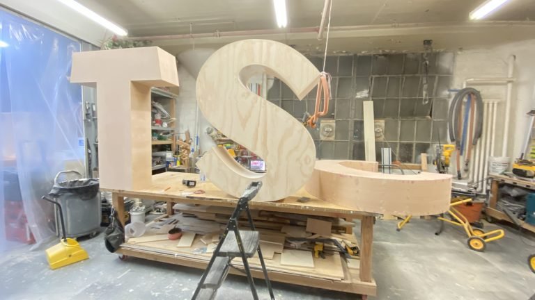 Large unfinished letters and a curved scenic component on a workshop bench.
