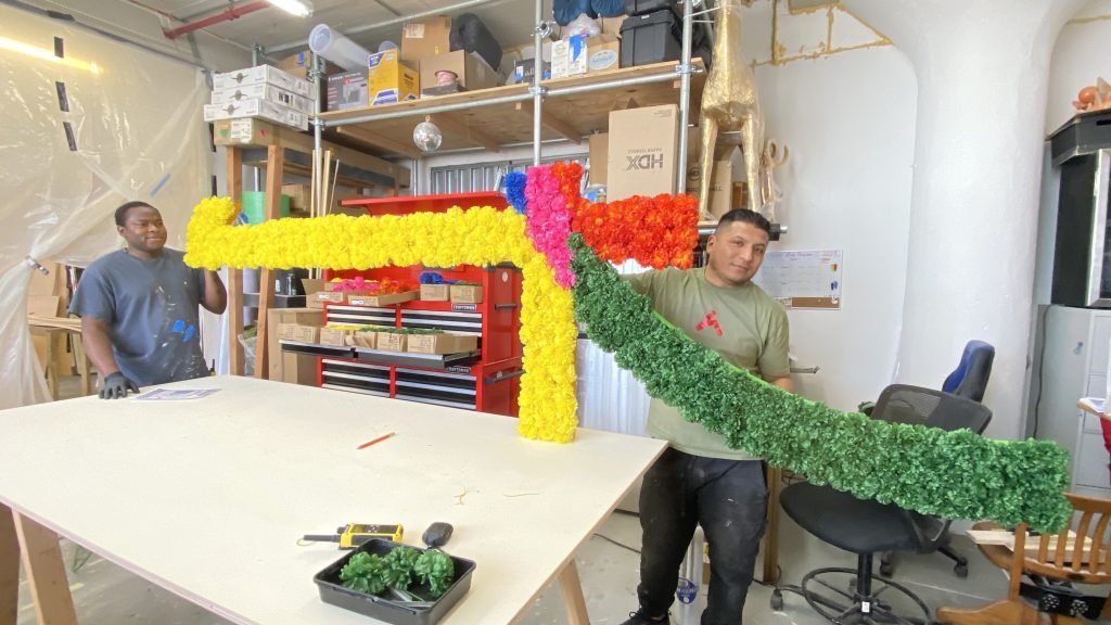 Workshop team holding curved and straight floral-covered scenic pieces.